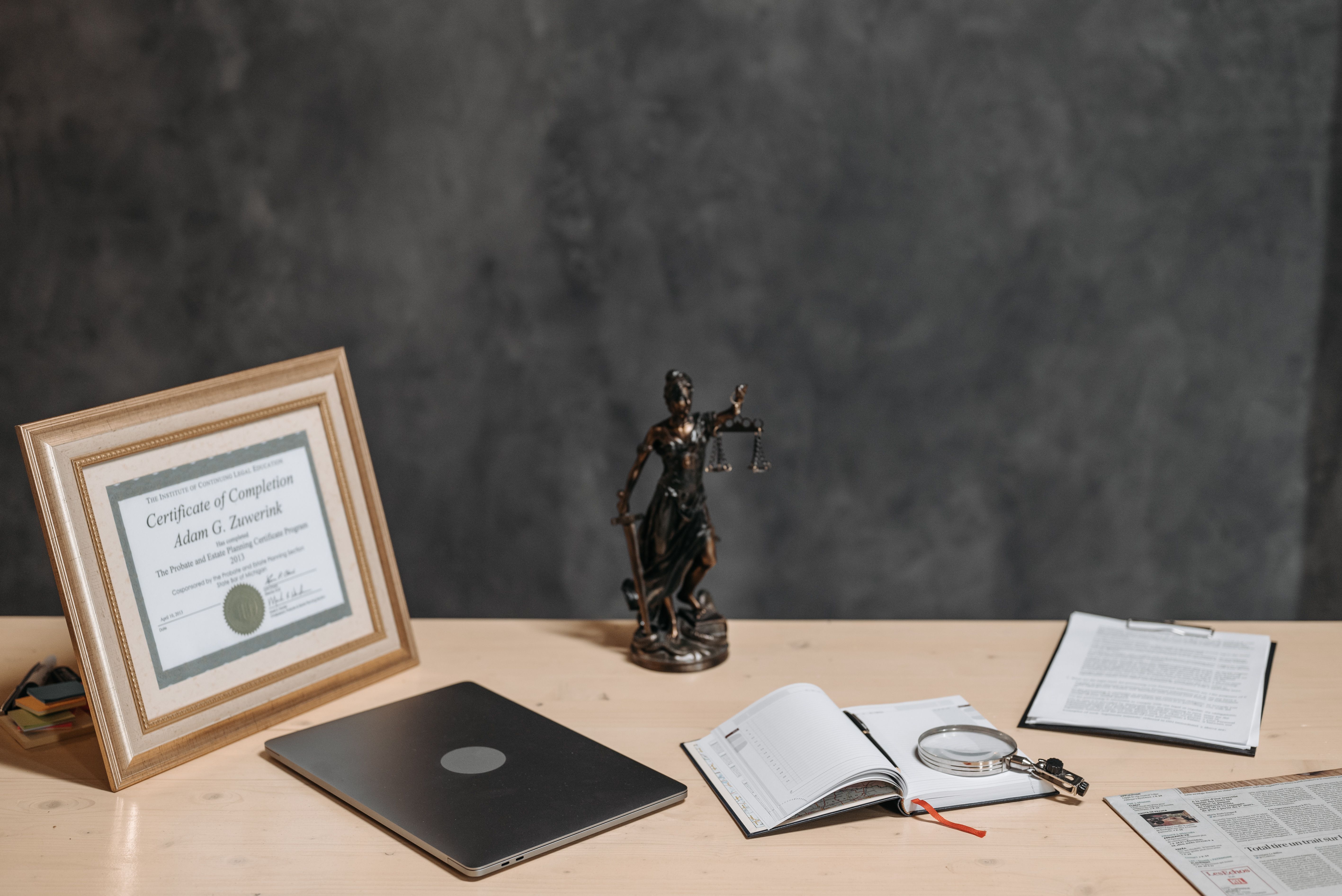 Lawyer's desk with Lady Justice, legal documents, laptop, and magnifying glass