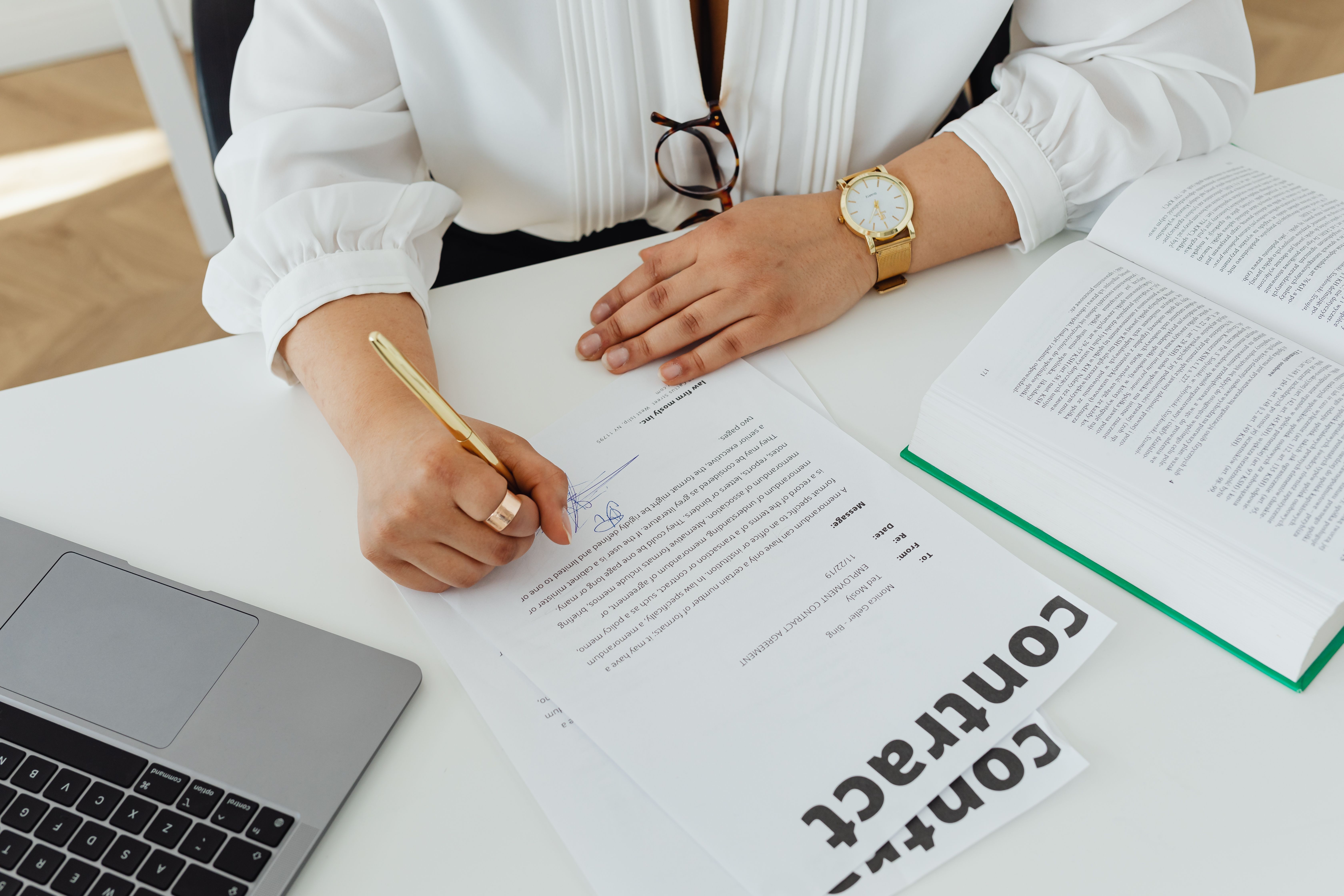 Businesswoman signing a legal contract at a desk with a laptop and documents